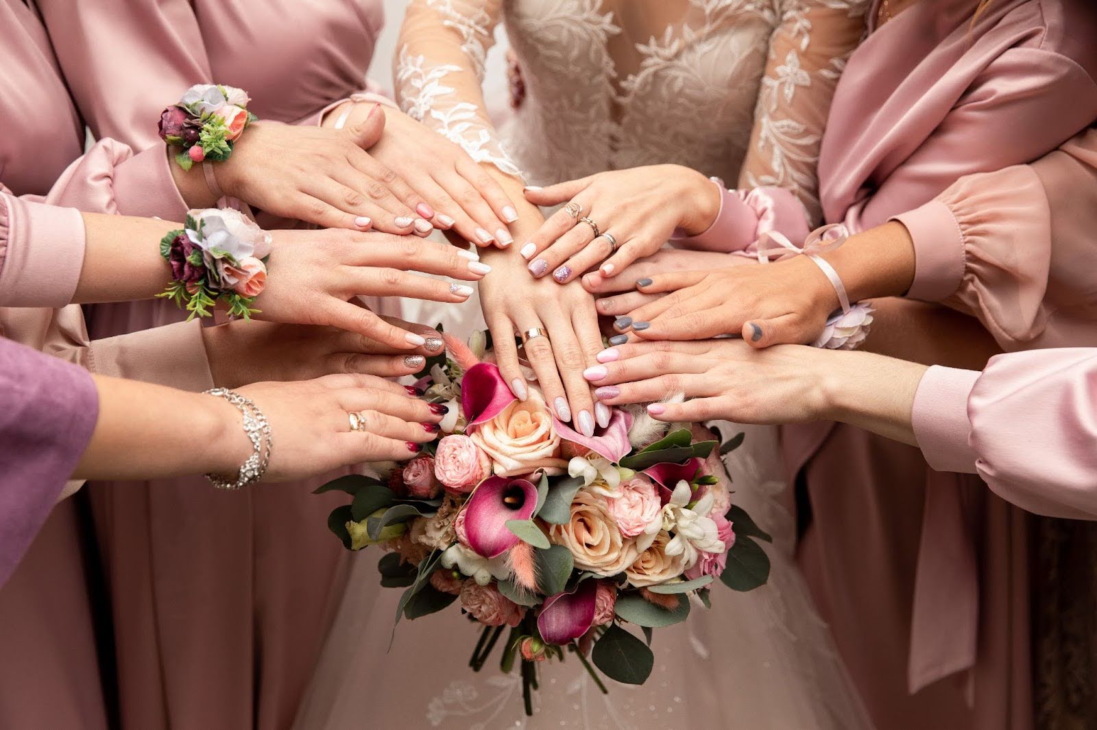 Bridesmaids and bride showing off pastel and neutral wedding nail designs around a pink floral bouquet.