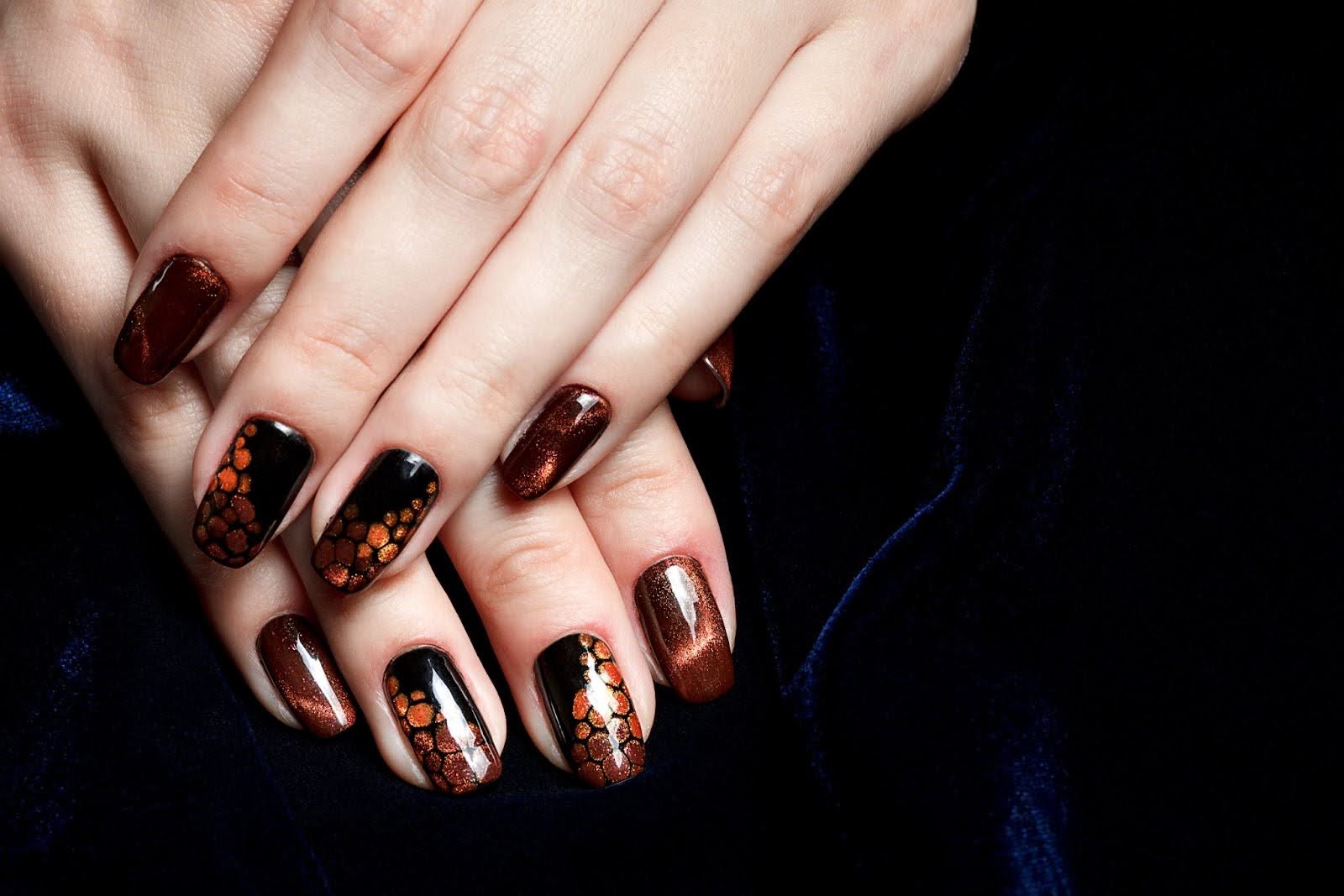 Hands with metallic brown and black cat eye nail art featuring a honeycomb-style hexagon pattern, displayed over dark navy velvet fabric.