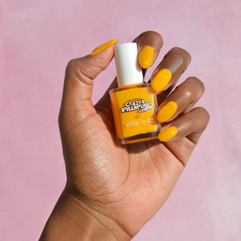 Gabby's Dollhouse Pillow Cat Sunshine yellow nail polish on a deep skin tone, hand holding the bottle