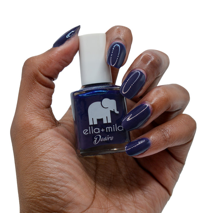 Bite Me deep vampy purple nail polish on a deep skin tone, hand holding the bottle