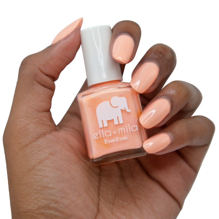 French Kiss peach coral nail polish on a deep skin tone, hand holding the bottle