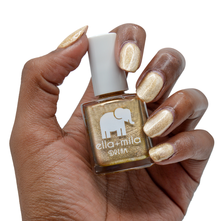 Gilded metallic gold nail polish on a deep skin tone, hand holding the bottle