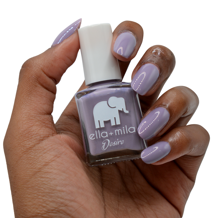 Mauve Over grey-purple nail polish on a deep skin tone, hand holding the bottle