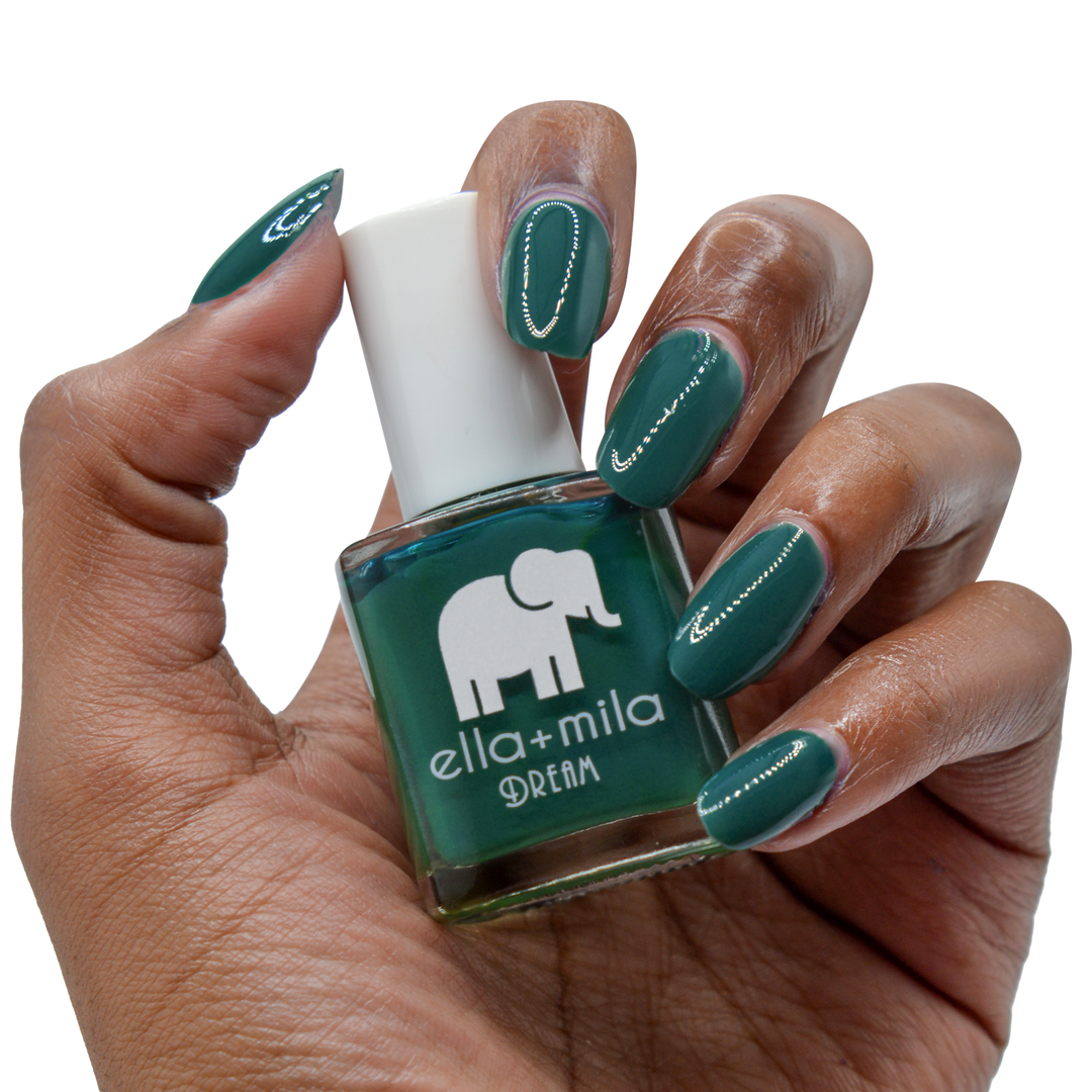 Mistletoe Magic dark green nail polish on a deep skin tone, hand holding the bottle
