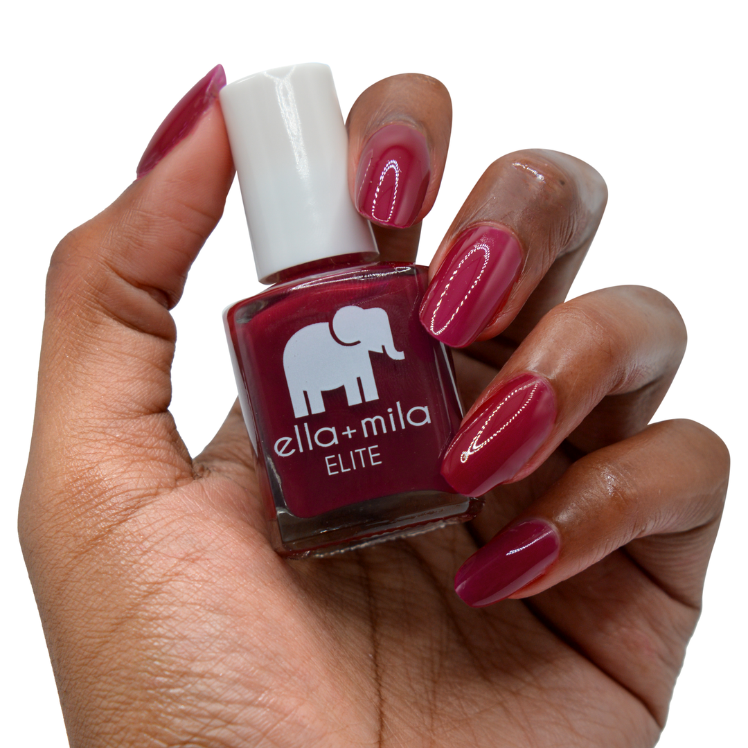 Naughty Not Nice ruby red nail polish on a deep skin tone, hand holding the bottle