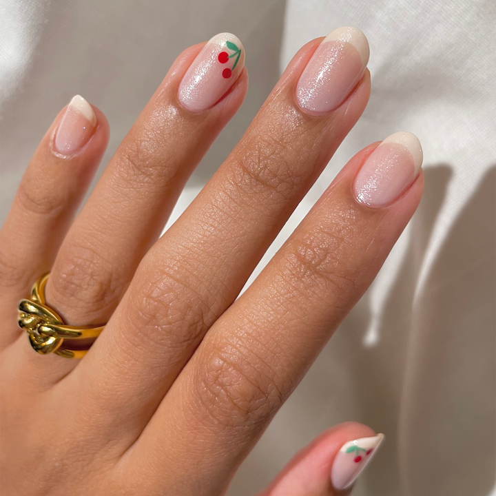Pixie Dust sheer shimmer nail polish with tiny red floral accents, hand with gold ring