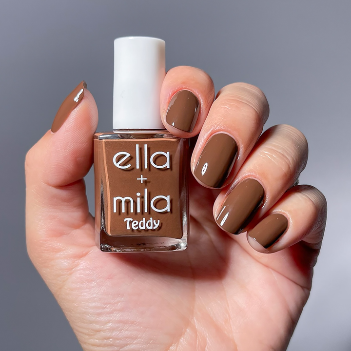 The Snuggle is Real cocoa brown nail polish manicure on a light skin tone, holding the bottle