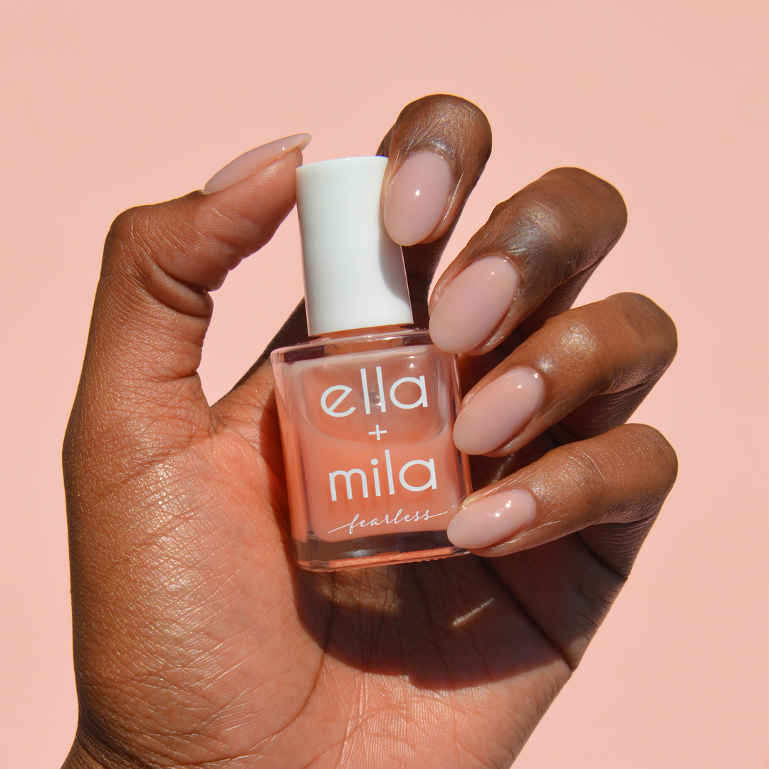 Unstoppable milky peach nail polish on a deep skin tone, hand holding the bottle