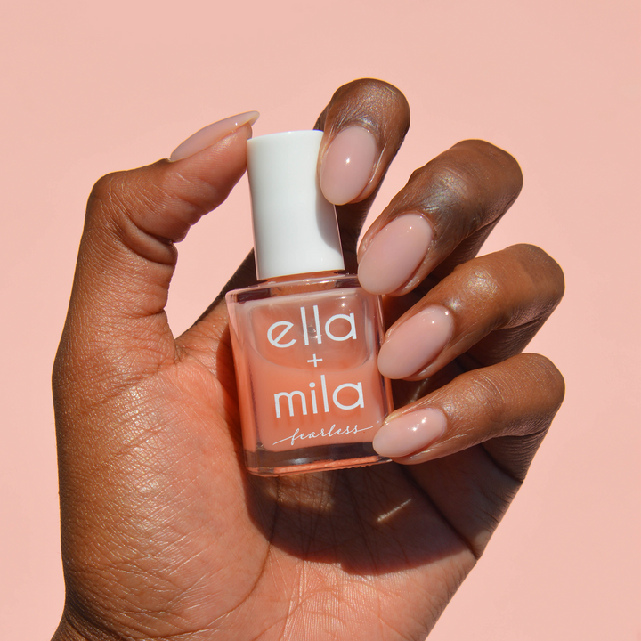 Unstoppable milky peach nail polish on a deep skin tone, hand holding the bottle