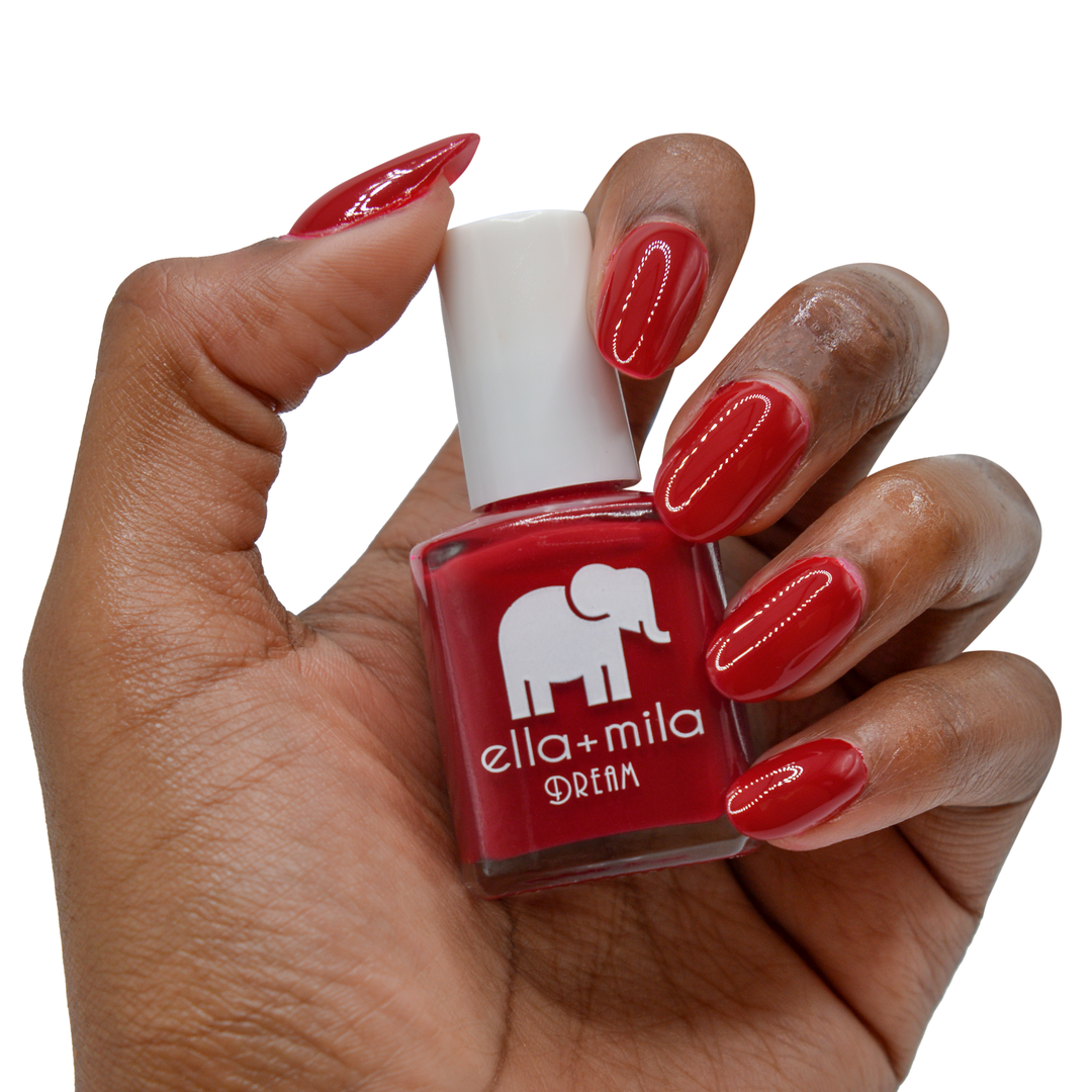 Unwrap Me pure red nail polish on a deep skin tone, hand holding the bottle
