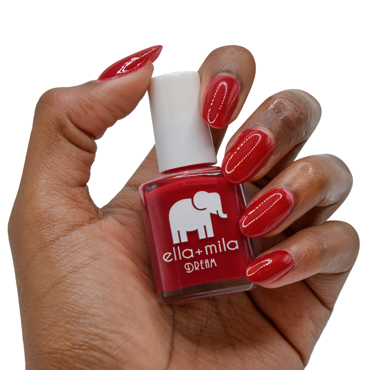 Unwrap Me pure red nail polish on a deep skin tone, hand holding the bottle