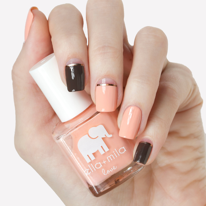 A Proposal peach nail polish with white and black accent nails, holding the bottle