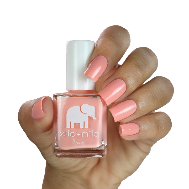 A Proposal peach coral nail polish on a medium skin tone, hand holding the bottle