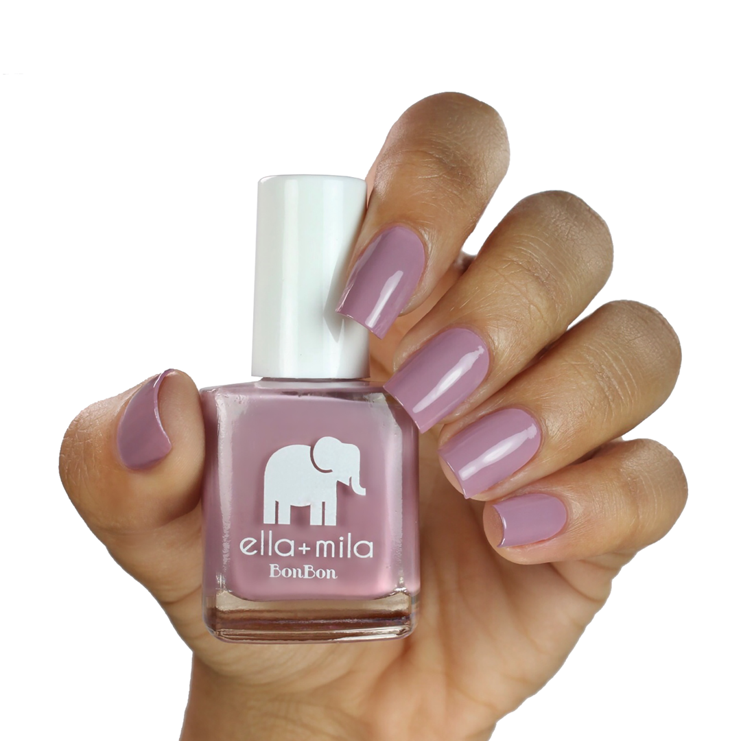 Dulce Amor dusty lavender rose nail polish on a medium skin tone, hand holding the bottle