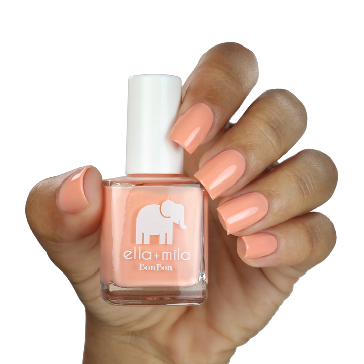 French Kiss peach pink nail polish on a medium skin tone, hand holding the bottle