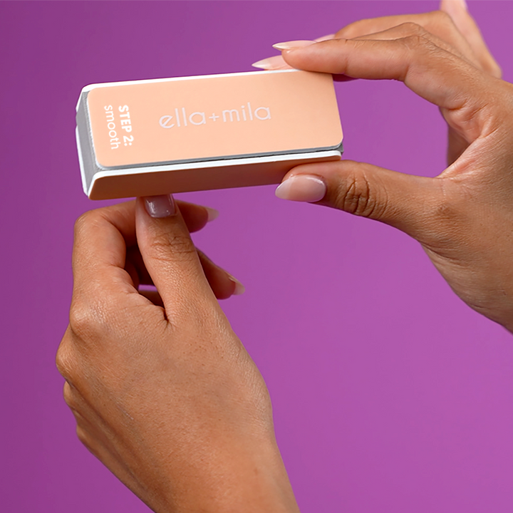 Hands using the peach nail buffer block on a purple background