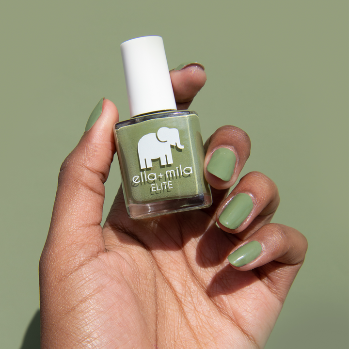 Paradise Isle army green nail polish on a deep skin tone, holding the bottle on a green background