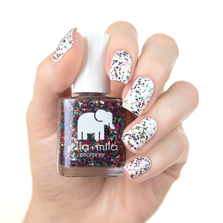 Party in a Bottle rainbow glitter nail polish over white nails, holding the bottle