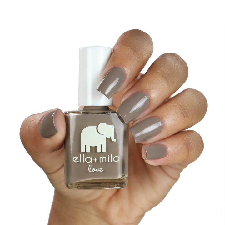 Sandstorm sandy grey brown nail polish on a medium skin tone, hand holding the bottle