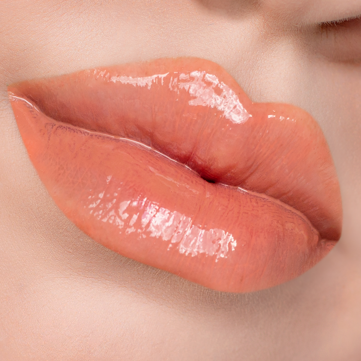 Strapless peach coral lip gloss on lips, light skin tone close-up