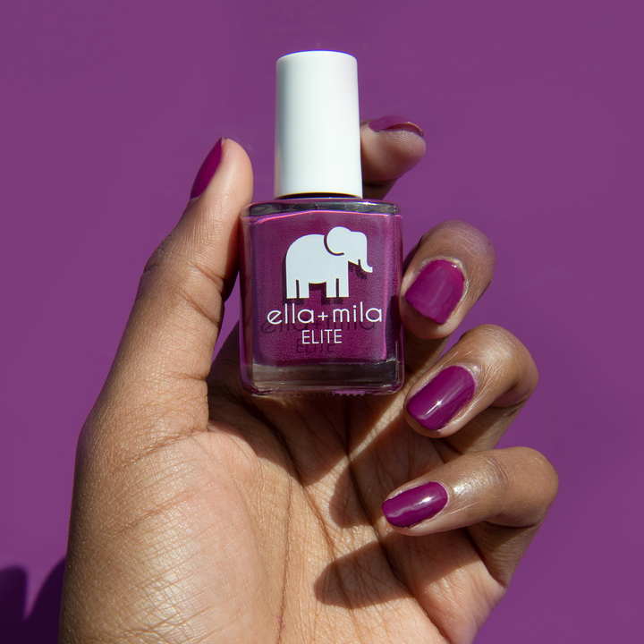 Take Off berry pink nail polish on a deep skin tone, holding the bottle on a purple background