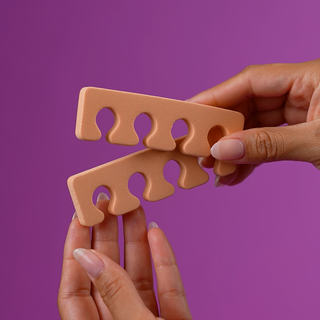Hand holding a peach foam toe separator on a purple background
