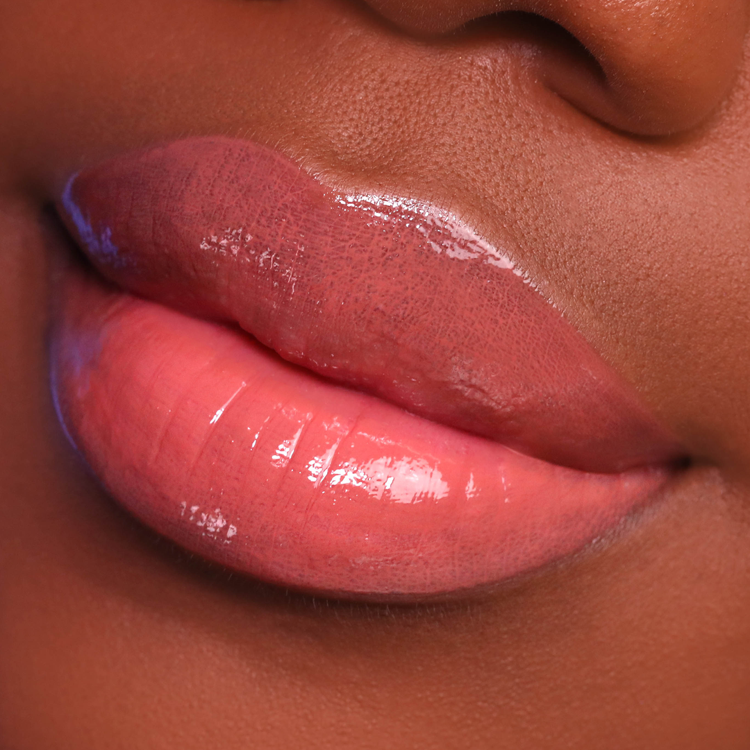 Vibes coral lip gloss on lips, deep skin tone close-up